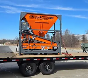 orange and grey Ultimate Bagger sandbag machine loaded on a flatbed trailer